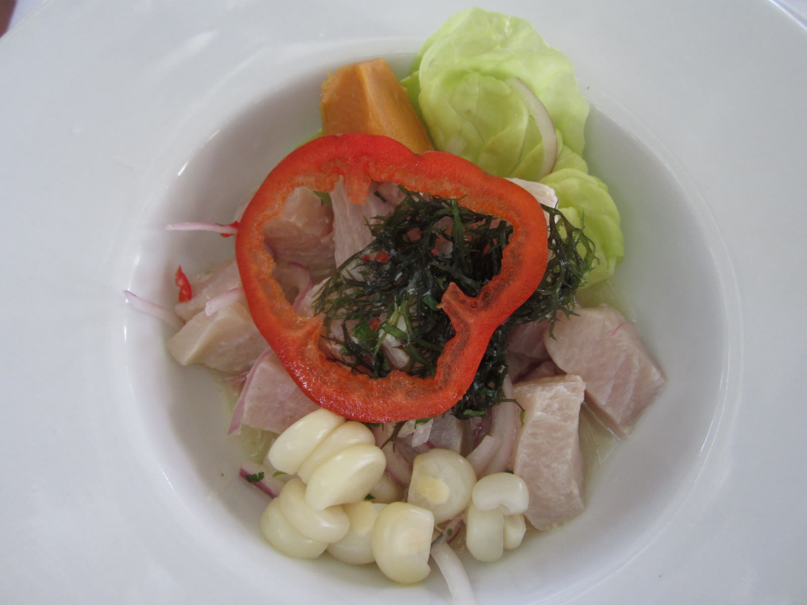 Ceviche clásico con choclo, camote, lechuga y ají en un plato blanco
