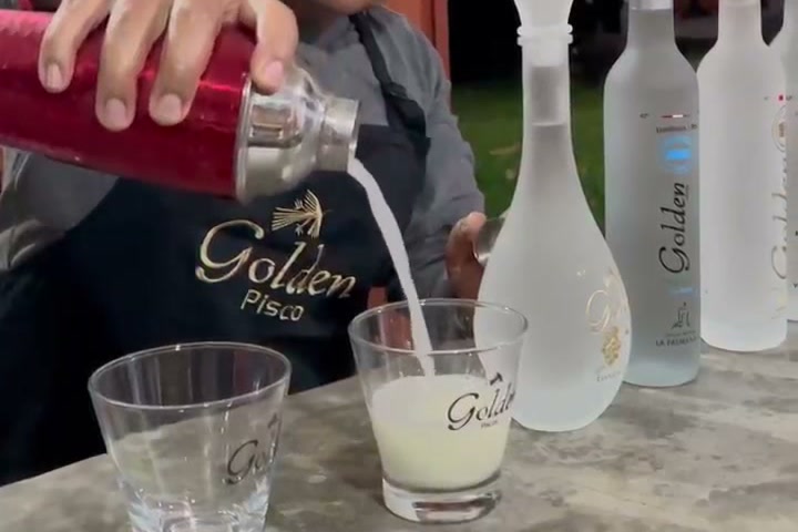 Un barman sirve un cóctel de pisco desde una coctelera roja en la barra de una bodega