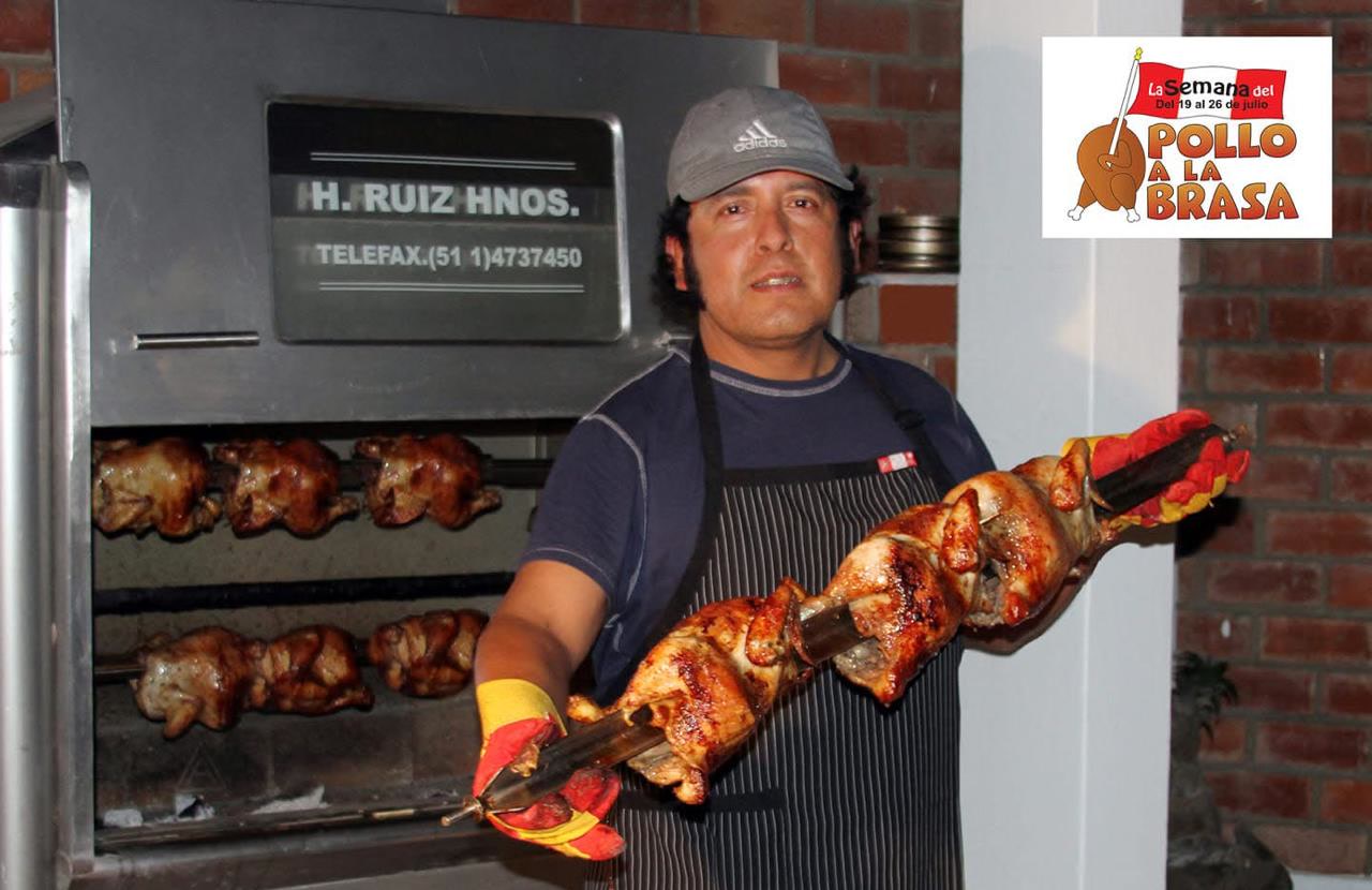 Cocinero sostiene una varilla cargada de pollos a la brasa frente al horno rotatorio, durante la Semana del Pollo a la Brasa