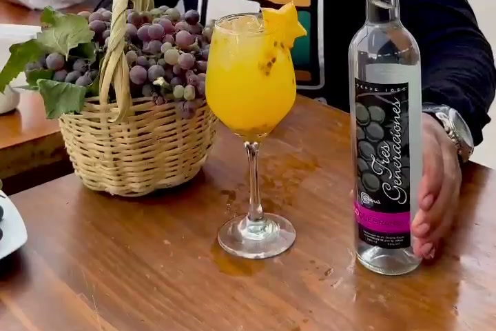 Canasta de uvas, copa de cóctel y botella de pisco sobre una mesa de madera en una bodega